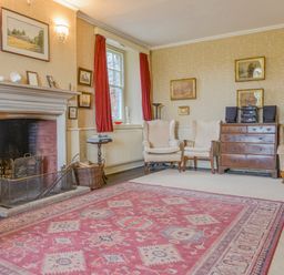 A sitting room with a fireplace three armchairs a wooden chest of drawers and a patterned rug at Wootton House in Butleigh Wootton near Compton Dundon