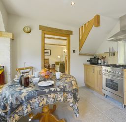 A kitchen with a table set for two and wooden cabinets at Pittards Farm Cottage in South Petherton