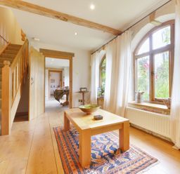 A hallway with wooden stairs a table on a rug and arched windows with curtains at Pittards Farm Cottage in South Petherton