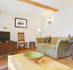 A living room with a sofa chair a television on a wooden cabinet and a green bowl on a wooden table at Pittards Farm Cottage in South Petherton