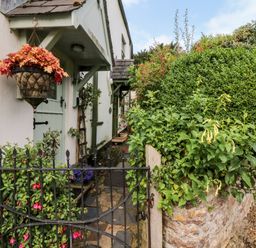 A stone pathway leading to a mint green door with a hanging basket and garden gate at Castle View in Dunster