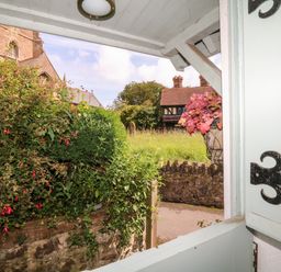 View through an open window showing bushes a stone wall and buildings outside at Castle View in Dunster