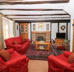 A living room with red upholstered seating a wooden coffee table a fireplace and a television at Castle View in Dunster