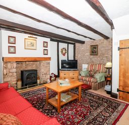 A living room with a red sofa a wooden coffee table a tv on a chest of drawers and stone walls at Castle View in Dunster