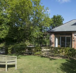 A garden with a wooden bench and hedges next to a brick building with a slate roof at Grooms Cottage in Talaton near Ottery St Mary