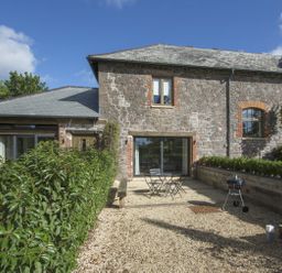 An outdoor patio area with a table and chairs a charcoal grill hedges and a stone house wall at Gardeners Cottage in Talaton near Ottery St Mary