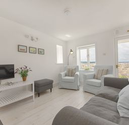 A living room with two armchairs a sofa a TV on a white stand and a door to the outside at 1 The Quay in Lympstone