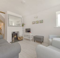 A living room with grey sofas a fireplace with a wood stove a white table with a small tv and a grey ottoman at 1 The Quay in Lympstone