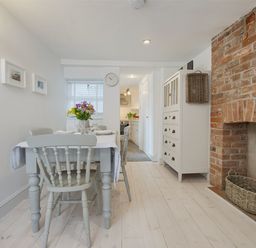 A dining area with a table and chairs a brick fireplace and a white cabinet at 1 The Quay in Lympstone