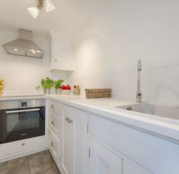 A kitchen with white cabinets a stainless steel oven and hood a sink and countertop with plants and fruit at 1 The Quay in Lympstone