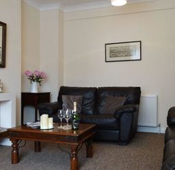 A living room with a leather sofa a wooden coffee table with glasses and candles and a fireplace at 2 Carlton Mews in Exmouth