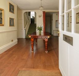 A hallway with wooden floor a wooden table with a flower vase and a staircase at Abbots Manor in Combe Raleigh near Honiton