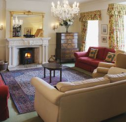 A living room with sofas armchairs floral curtains a fireplace and a chandelier at Abbots Manor in Combe Raleigh near Honiton