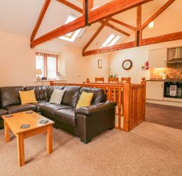 An open living room and kitchen with a brown leather sofa wooden coffee table wooden beams and dining table at The Old Stable in Sidbury near Sidmouth