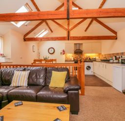 An open plan living area with a leather sofa and cushions a wooden dining table and a kitchen with white cabinets at The Old Stable in Sidbury near Sidmouth