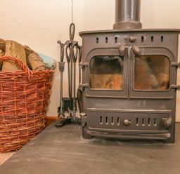 A wood burning stove with fireplace tools and a basket of firewood at The Old Stable in Sidbury near Sidmouth