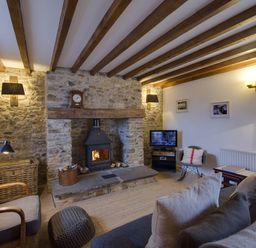 A living room with a stone fireplace wood burning stove chairs and a television at Whitcombe Cottage in Honiton