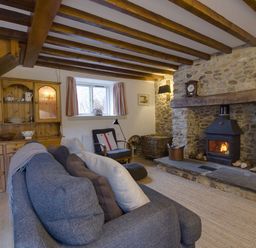 A living room with a stone fireplace wood stove wooden cabinet armchair and sofa at Whitcombe Cottage in Honiton