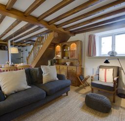 Living room with grey sofas and armchair near a window and wooden cabinet with stairs in background at Whitcombe Cottage in Honiton