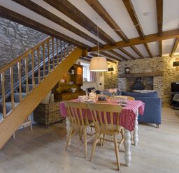 A dining table with a red checkered tablecloth and wooden chairs under a wooden beam ceiling in a room with stone walls and a fireplace at Whitcombe Cottage in Honiton