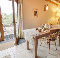 A dining room with a wooden table set with mugs plates and eggs next to glass doors leading to a patio at Swallows Cottage in Honiton