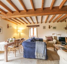 A living room with wooden beams a dining table wooden chairs blue sofa armchairs and a stone fireplace at Swallows Cottage in Honiton