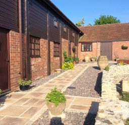 A brick and wood exterior courtyard with potted plants and large urns at The Linney in Colyton