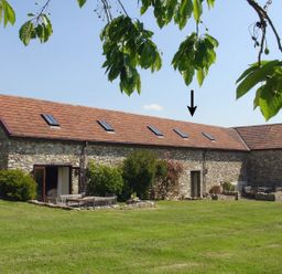 An exterior view of a stone barn with a tiled roof and outdoor seating on grass at The Linney in Colyton