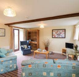 A living room with patterned sofas a wooden bookshelf and a small television at The Linney in Colyton
