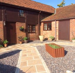 A courtyard with brick walls and wooden doors and windows with plants in pots at Battens in Colyton