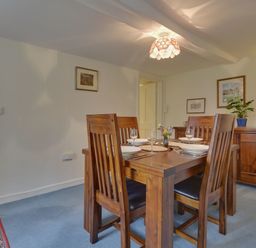 A dining room with wooden table and chairs set for four with plates and wine glasses at Lew Quarry Cottage in Lewdown