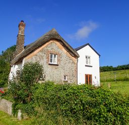 A thatched roof cottage with brick chimney and garden hedge at West Henstill House in Sandford Devon
