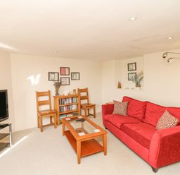 A living room with a red sofa wooden coffee table wooden chairs and television at West Henstill House in Sandford Devon