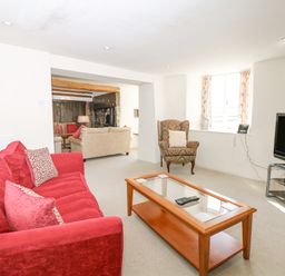 A living room with a red sofa a wooden coffee table an armchair and a television at West Henstill House in Sandford Devon