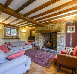 A living room with wooden beams and a stone fireplace with a wood stove at Hope Cottage in Riddlecombe near Winkleigh
