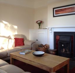 A living room with beige sofas a wooden coffee table a fireplace and a basket of firewood at Hedgelea in North Tawton