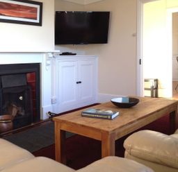A living room with a fireplace television on cabinet wooden coffee table and leather sofas at Hedgelea in North Tawton