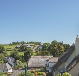 Houses with thatched roofs and a stone church tower in a village with trees and fields at Linney Cottage in Dittisham