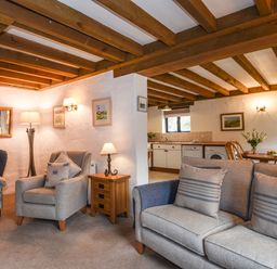 A living room with armchairs and a sofa next to a kitchen and dining area at Bramble Cottage in Ringmore