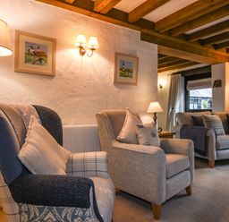 A living room with armchairs a sofa lamps framed pictures and wooden ceiling beams at Bramble Cottage in Ringmore