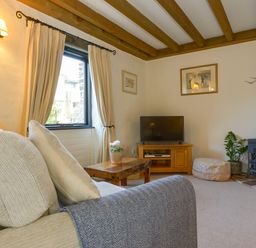 A living room with a sofa pillows coffee table television and a stove at Bramble Cottage in Ringmore