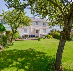 A garden with a lawn trees and a picnic table in front of a two story house at 4 Coastguards Cottage in Hope Cove