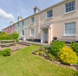 A row of pastel-colored terraced houses with outdoor benches a barbecue grill a picnic table and a garden at 4 Coastguards Cottage in Hope Cove