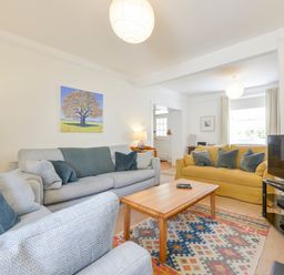 A living room with sofas cushions a wooden coffee table a patterned rug a television and a painting of a tree on the wall at 4 Coastguards Cottage in Hope Cove
