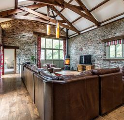 A living room with a large brown leather sofa a wood burning stove and a television on a wooden stand at Mill Barn in Woolston near Salcombe