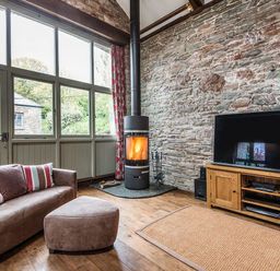 A living room with a wood burning stove a sofa and a television at Mill Barn in Woolston near Salcombe