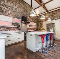 A kitchen with stone walls a large island with colorful stools and hanging lights at Mill Barn in Woolston near Salcombe