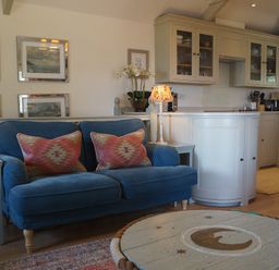 A living room with a sofa and kitchen area at Coach House Cottage, Strete, near Dartmouth