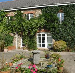 An outdoor courtyard with a stone building covered in ivy and a small water fountain surrounded by potted plants at The Gallery in Aveton Gifford