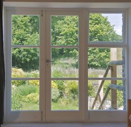 A window with glass panes overlooking a garden with green trees at The Gallery in Aveton Gifford
